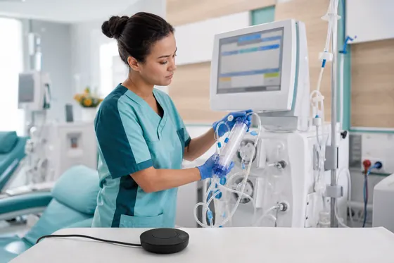 Dialyseverpleegkundige bedient dialyseapparatuur bij een behandelstoel